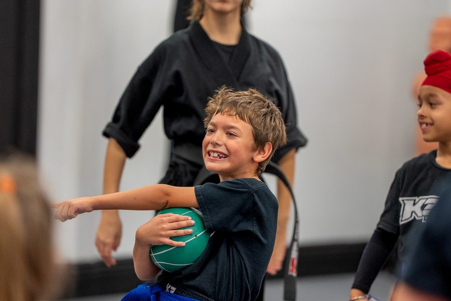 Young K3 student laughing while playing a ball game on the mat